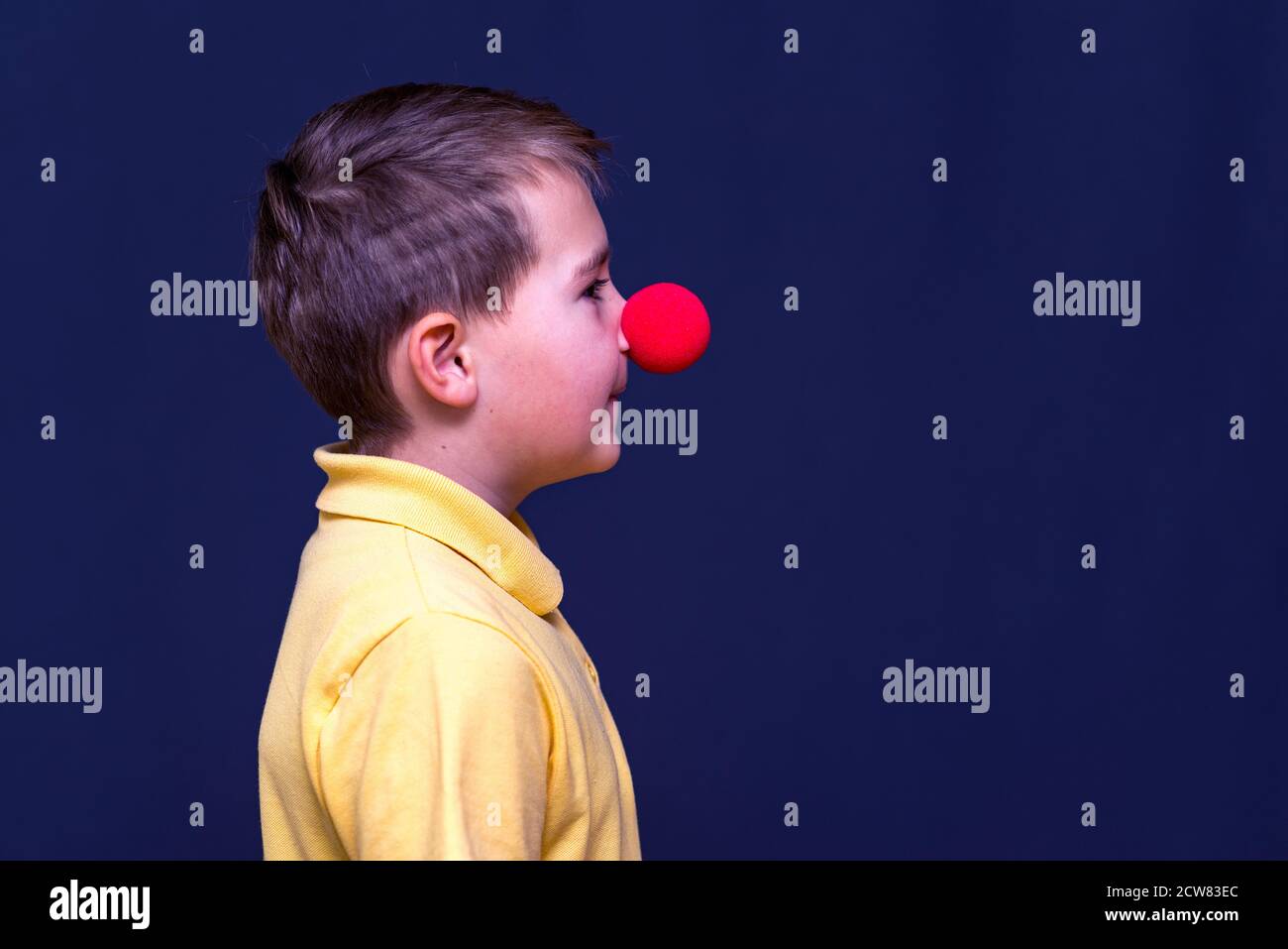 Side view Portrait of child boy wearing yellow t shirt clown nose,red nose concept. Stock Photo