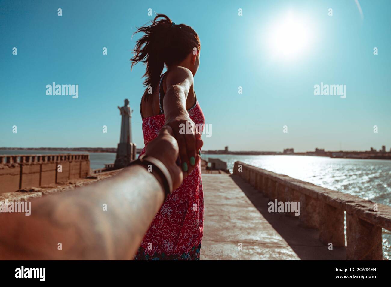 Follow me. Young woman holding hand and leading man to the beautiful nature sunset yellow landscape. View from back side, POV. Romantic couple travel Stock Photo