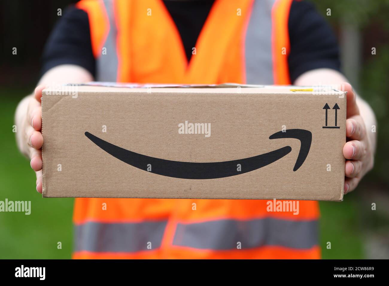 A man delivering an Amazon box with the Amazon smile logo in the UK Stock Photo