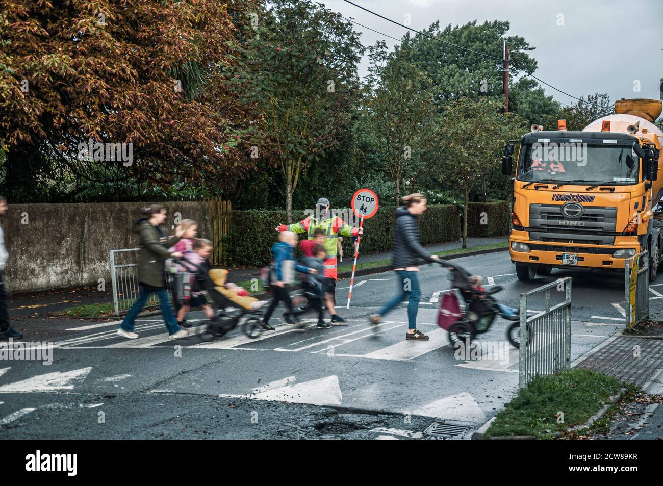 Everyday life. School run: Mums walking kids to school at road crossing with help of crosswalk attendant. Greystones. Ireland. Stock Photo