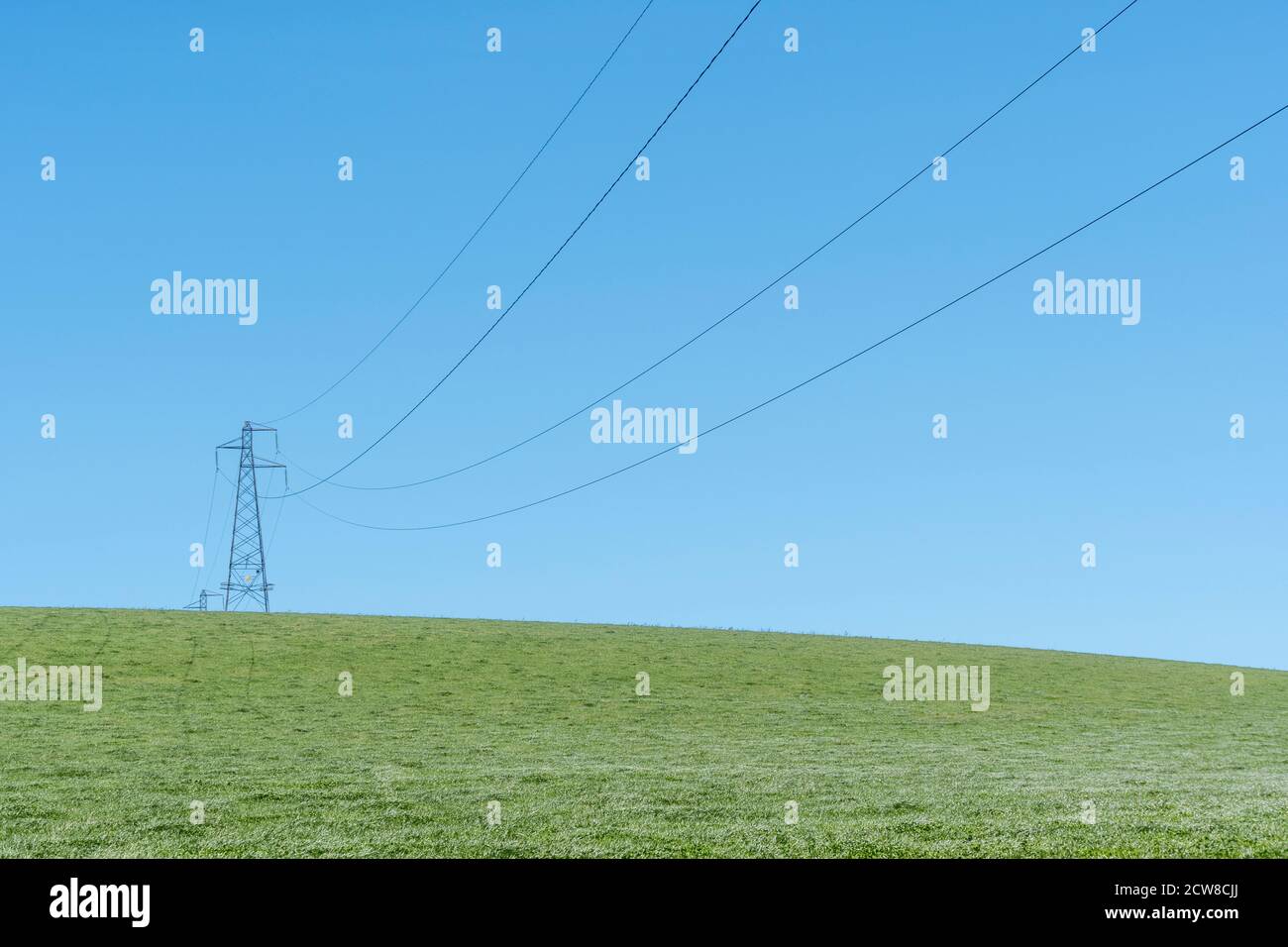 High voltage electricity pylon in field set against blue summer sky