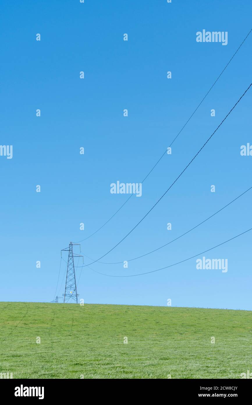High voltage electricity pylon in field set against blue summer sky