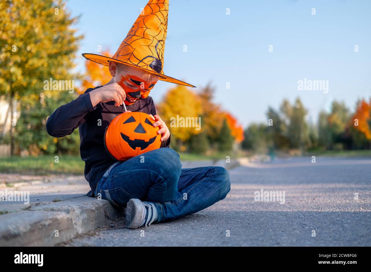 Halloween kids. boy with pumpkin face mask in witch costume hat eating ...
