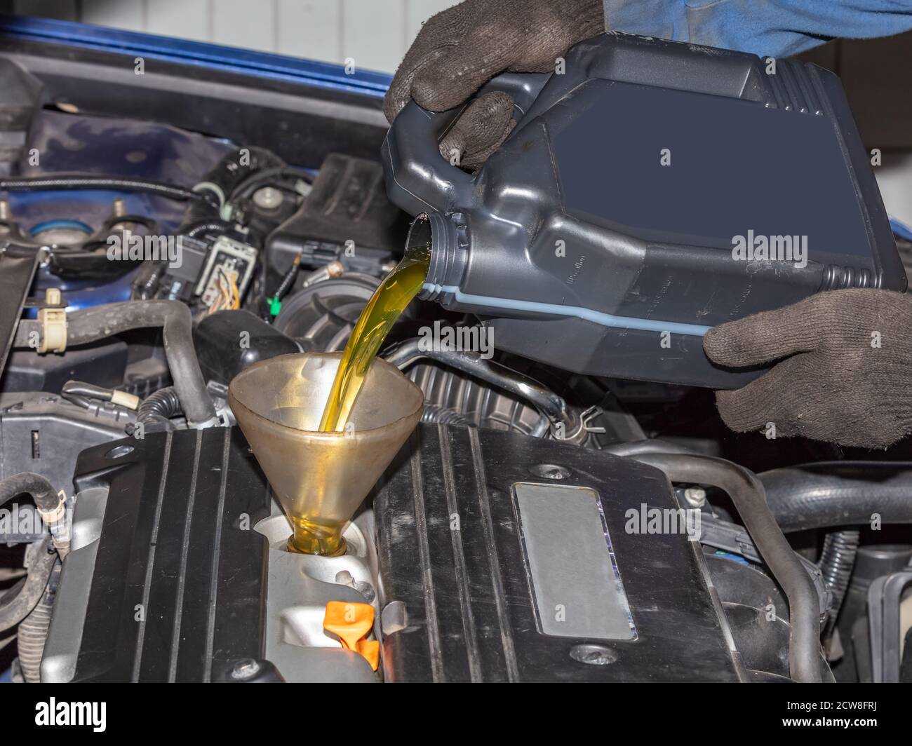 Mechanic topping up the oil in a car pouring a pint of oil through a