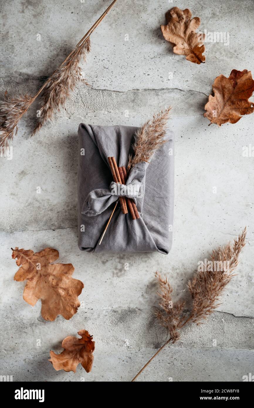 Top view of wrapped gifts by linen fabric in furoshiki eco style with Autumn decor. Thanksgiving or Halloween celebration concept. Stock Photo