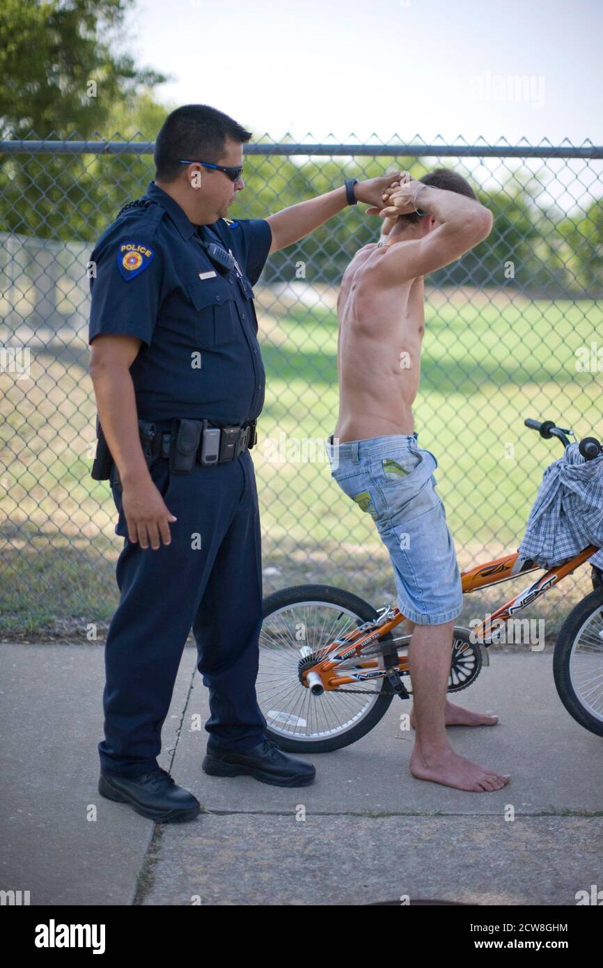 Round Rock, Texas: July 20, 2008: Hispanic police officer checks out a suspicious young man riding a bicycle near an elementary school. ©Bob Daemmrich Stock Photo