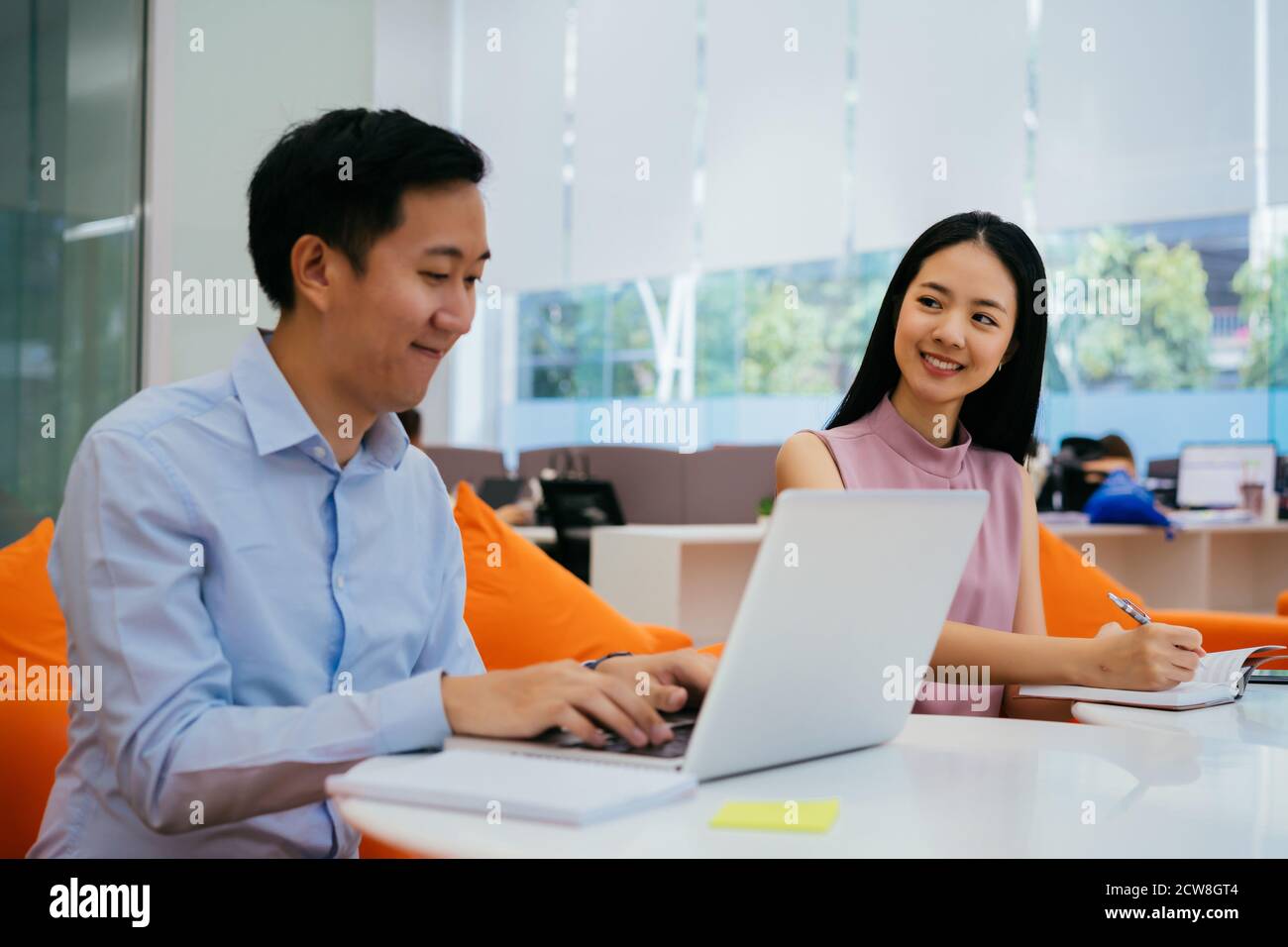 Asian businessman and woman smiling and working together, writing in notebook, collaboration, cooperation, teamwork Stock Photo