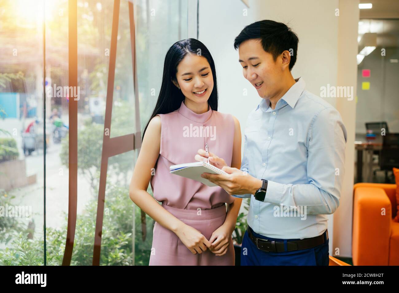 Asian businessman and woman smiling and working together, writing in notebook, collaboration, cooperation, teamwork Stock Photo