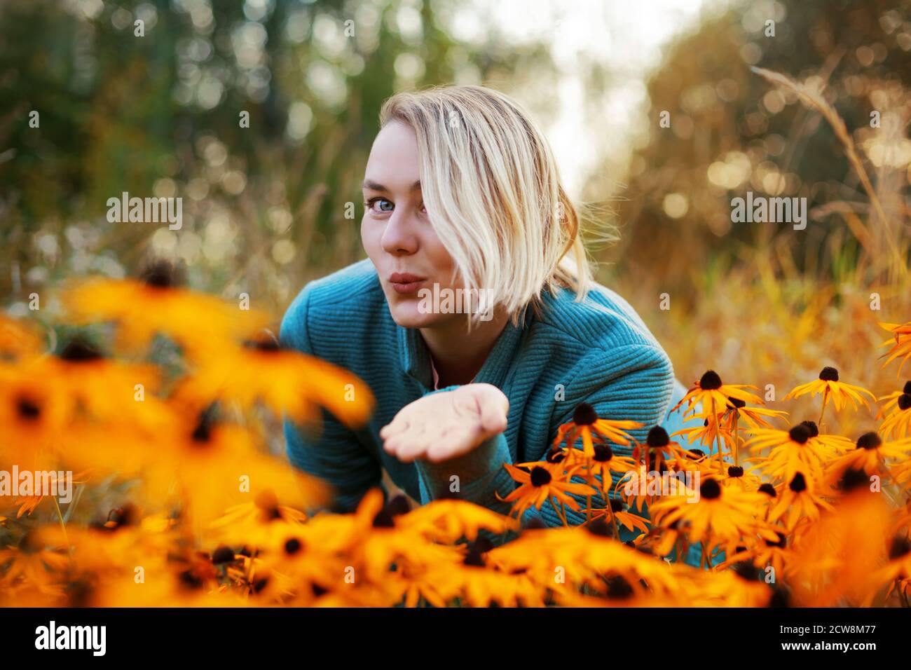 blonde caucasian female with bob haircut blows kiss. Autumn woman portrait with bright orange flowers Stock Photo