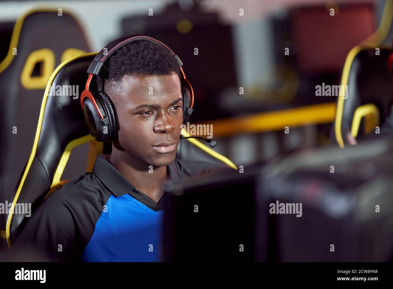 Portrait of focused african cybersport male gamer wearing headphones playing video games, participating in eSport tournament while sitting in gaming club or internet cafe Stock Photo