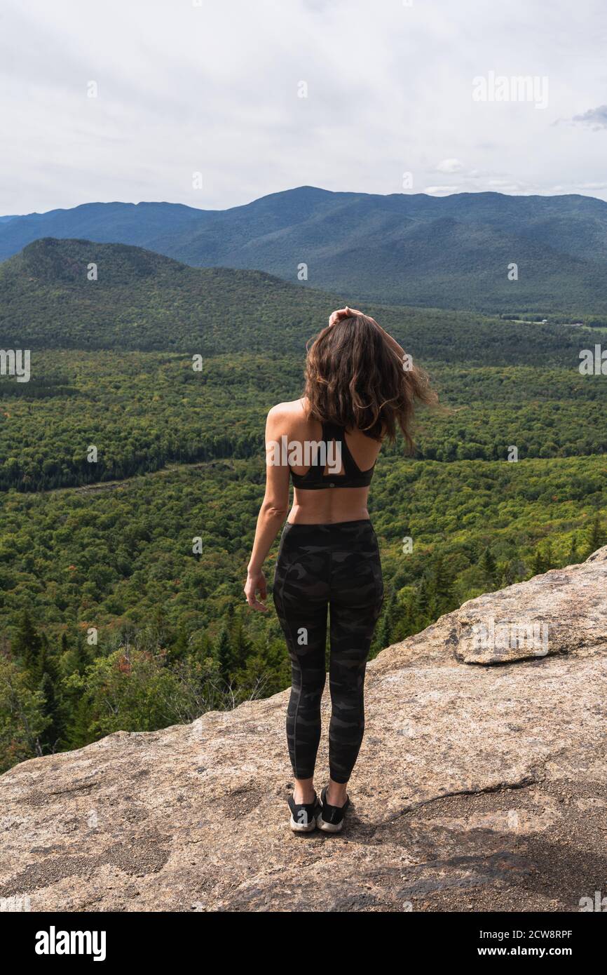 A young woman standing at the top of a mountain, looking out at the ...