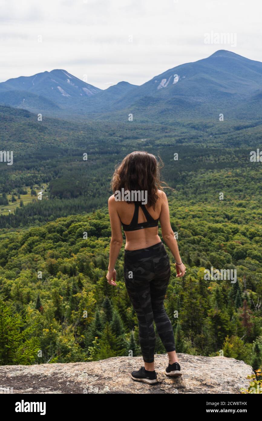 A young woman standing at the top of a mountain, looking out at the ...