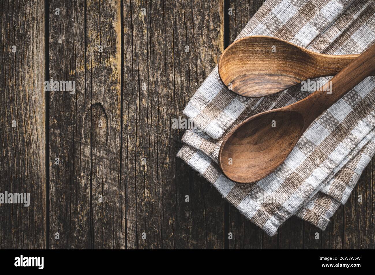 Two wooden spoons on checkered napkin on old wooden table. Top view. Stock Photo