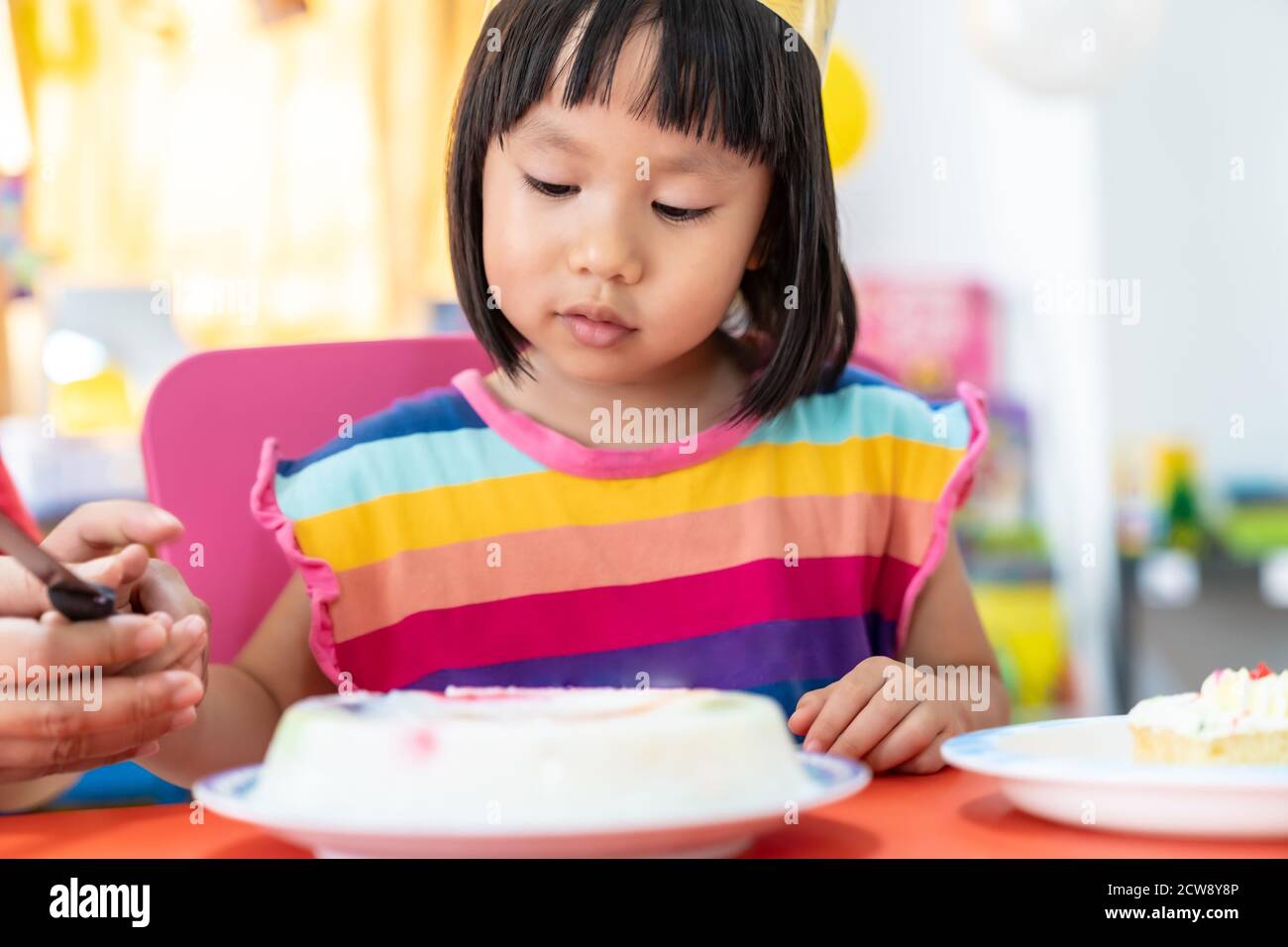 Asian girl kid cutting her birthday cake celebrate with mom alone because city lockdown while COVID-19 Pandemic. Celebration and quarantine concept. Stock Photo