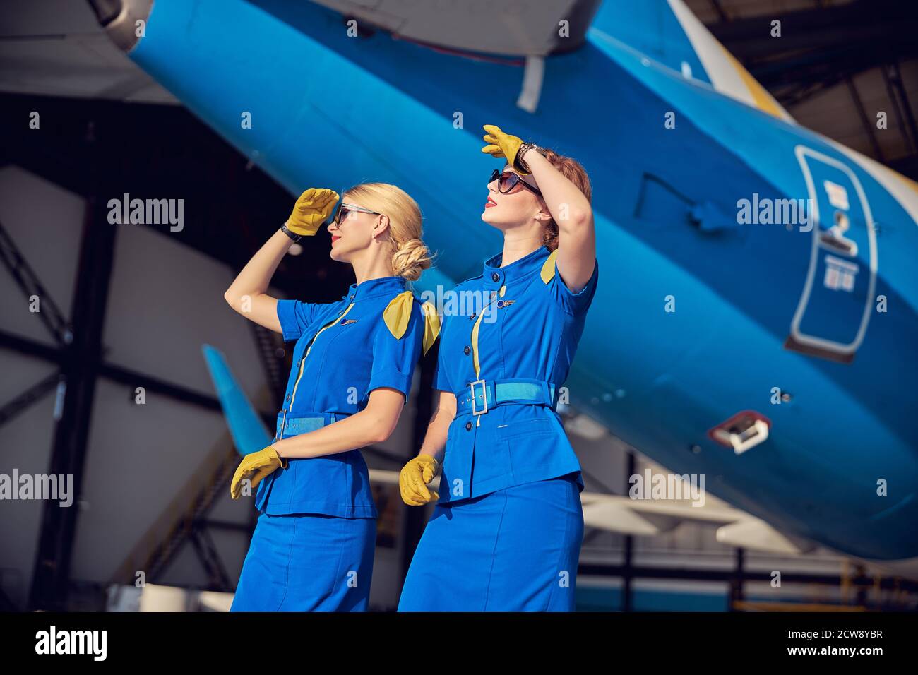 Good looking women air stewardesses in blue respective uniform and leather  gloves standing in front on big passenger airplane Stock Photo - Alamy