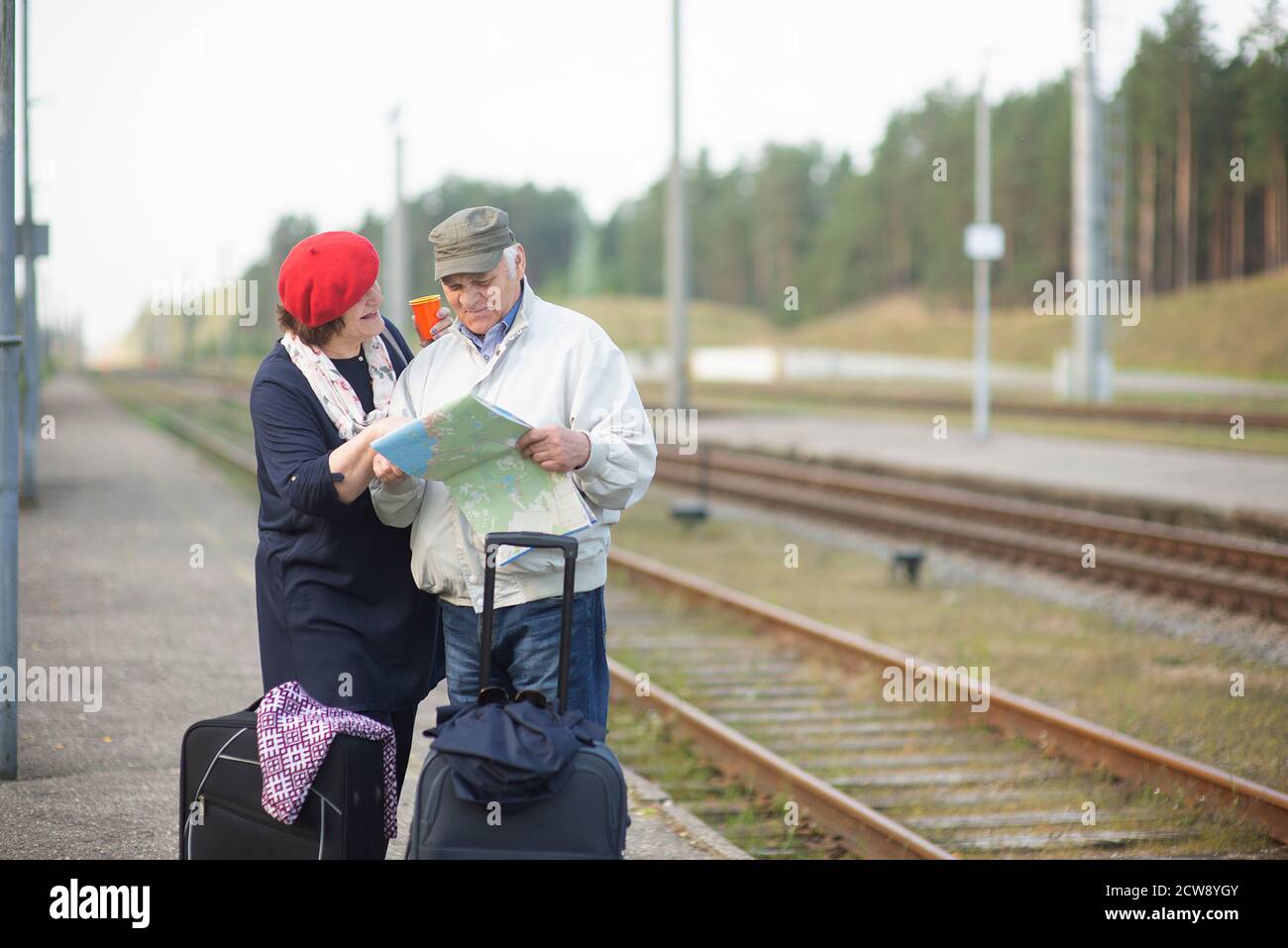 happy senior couple with suitcases looking at the map and waiting for the train to go on a trip Stock Photo