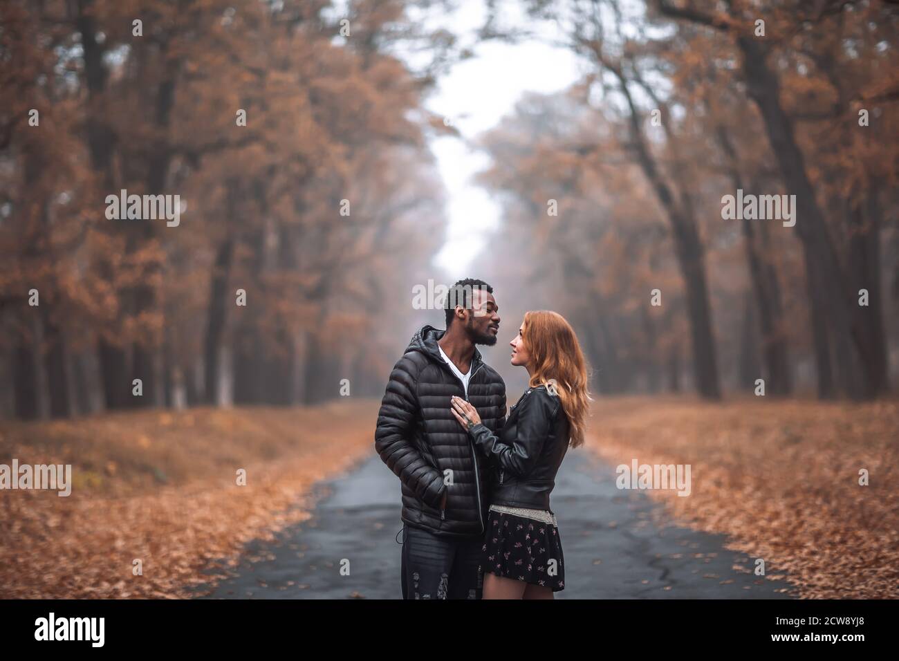 Interracial couple posing in autumn park road, black man and white redhead woman Stock Photo