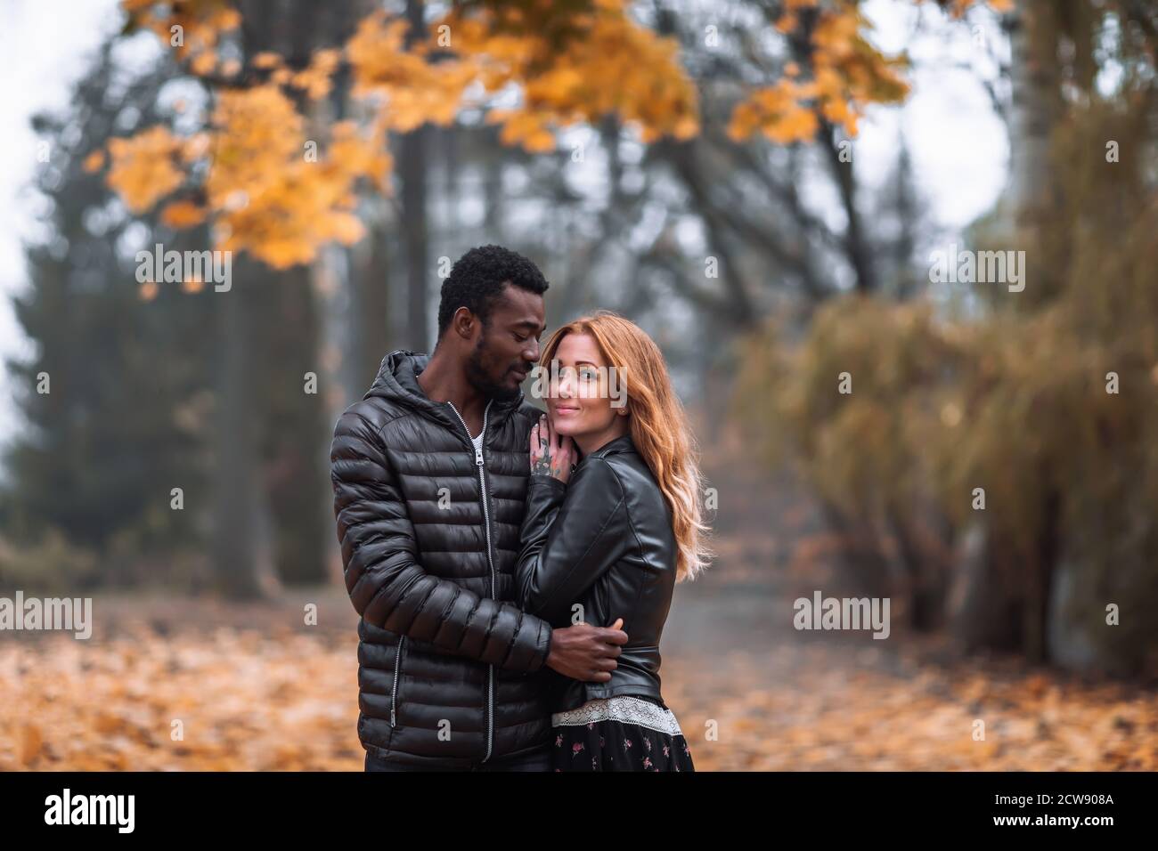 Happy cute Interracial couple posing in blurry autumn park background, black man and white redhead woman Stock Photo
