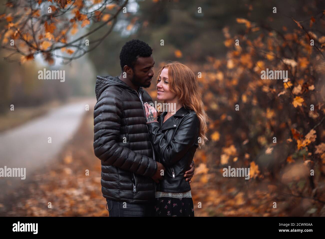 Happy cute Interracial couple posing in blurry autumn park background, black man and white redhead woman Stock Photo