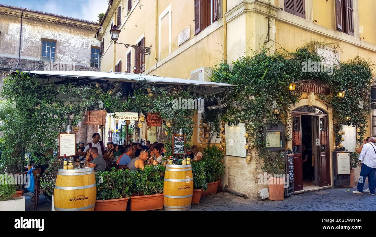 Tourists enjoy lunch at a picturesque sidewalk Italian cafe covered with ivy in the Trastevere district of historic Rome, Italy Stock Photo