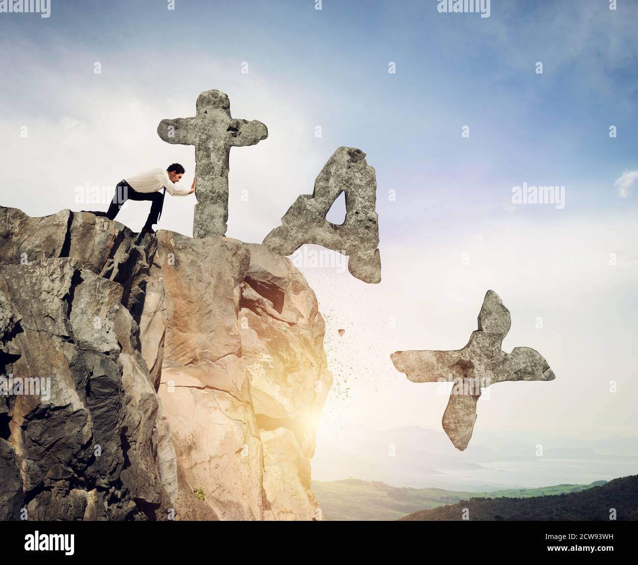 Businessmanthrows off the mountain the word TAX made of heavy rock Stock Photo