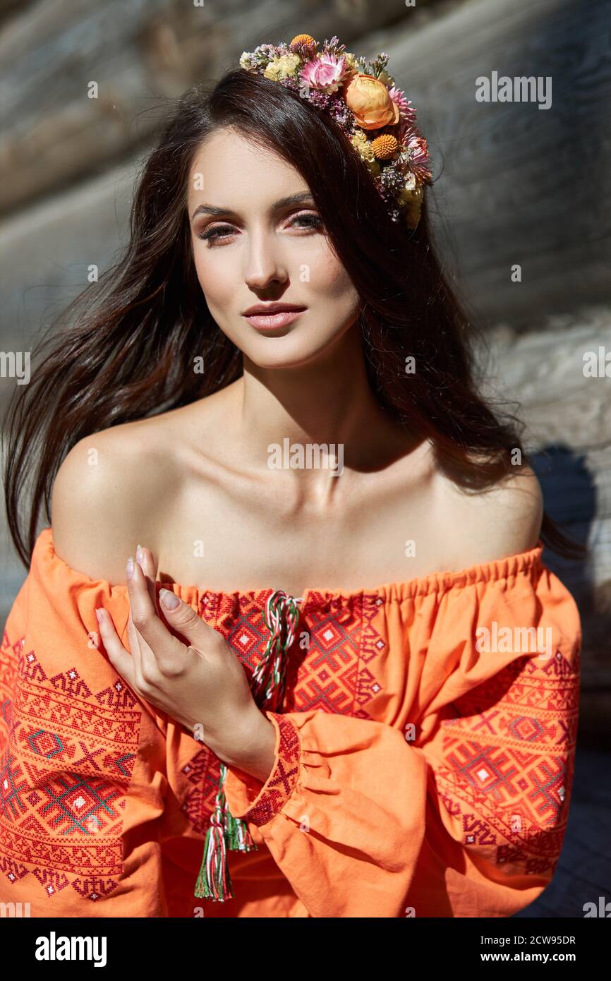 Beautiful Slavic woman in an orange ethnic dress and a wreath of flowers on  her head. Beautiful natural makeup. Portrait of a Russian girl Stock Photo  - Alamy