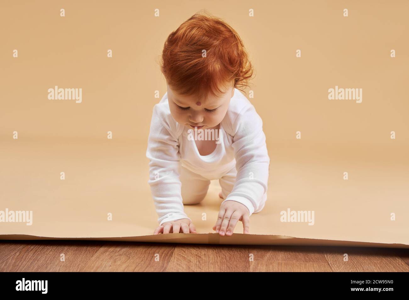 Little red-haired baby girl is playing on a beige background. Big mole on the forehead, not like everyone else Stock Photo