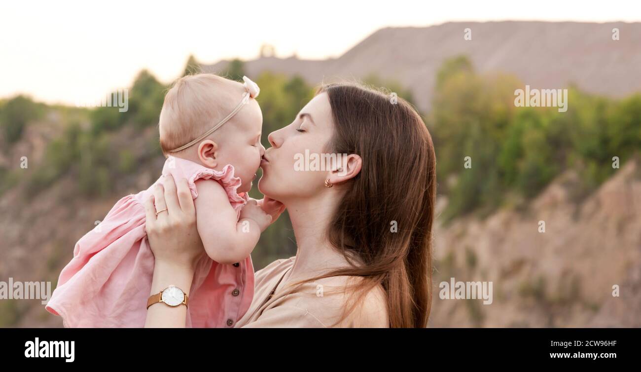Mom holds a child in her arms and kisses him gently on the cheek outdoor. Mom and daughter. Family concept. Stock Photo