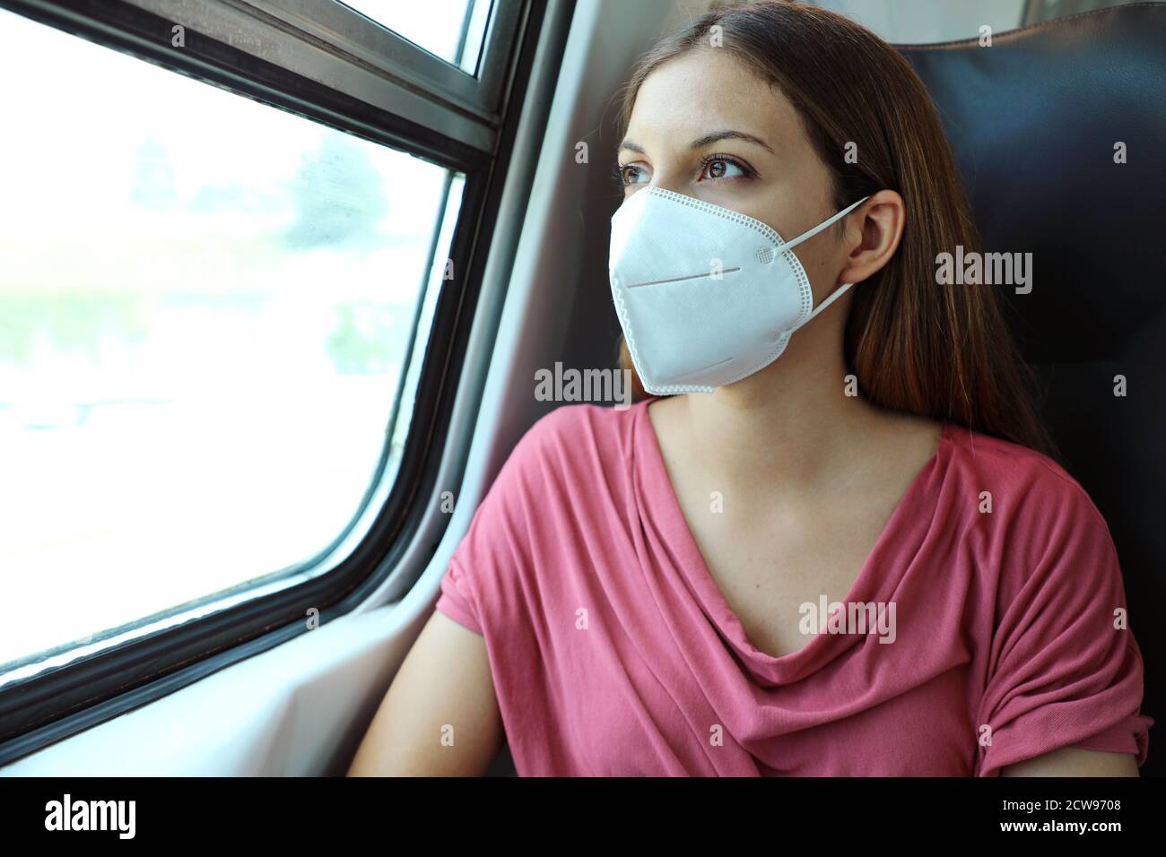 Travel safely on public transport. Young woman with KN95 FFP2 face mask looking through train window. Train passenger with protective mask. Stock Photo