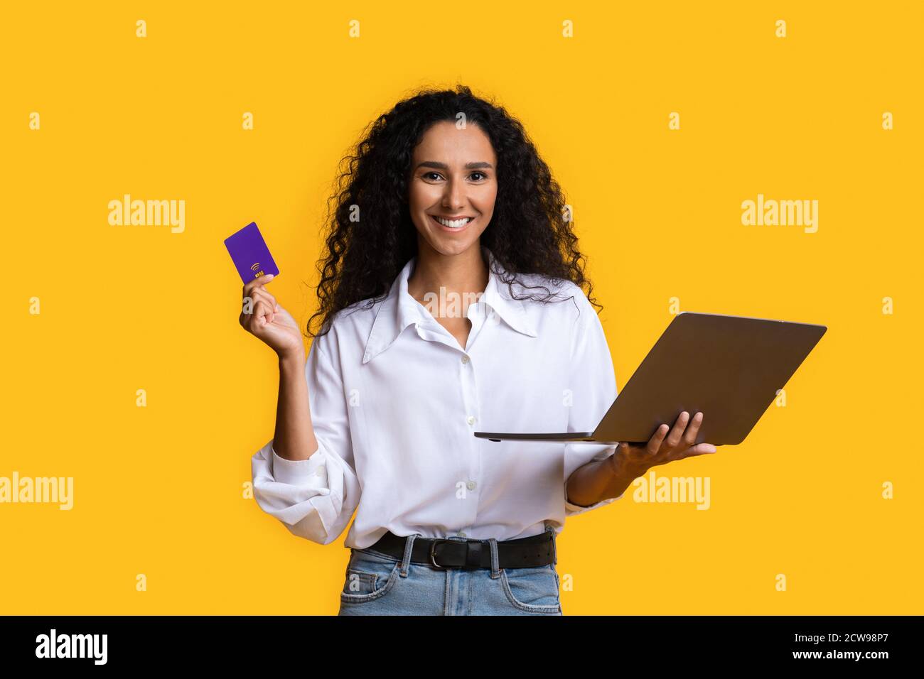 Online Payments. Happy woman with credit card and laptop over yellow background Stock Photo