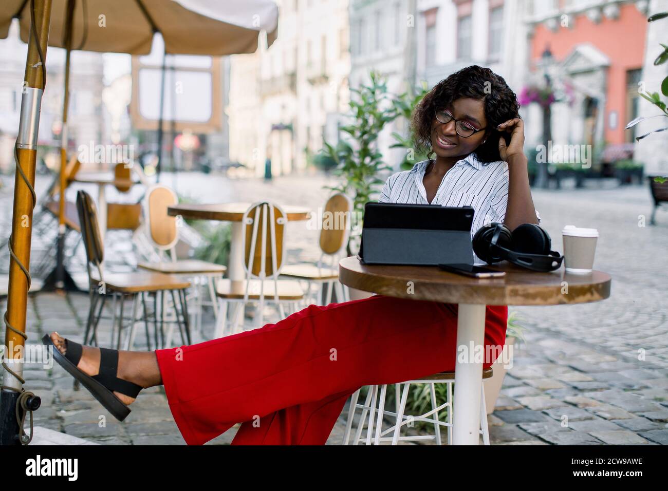 Portrait of a happy young african woman wearing smart casual clothes, red  pants and striped shirt, relaxing in outdoor cafe and using a tablet. Lunch  Stock Photo - Alamy