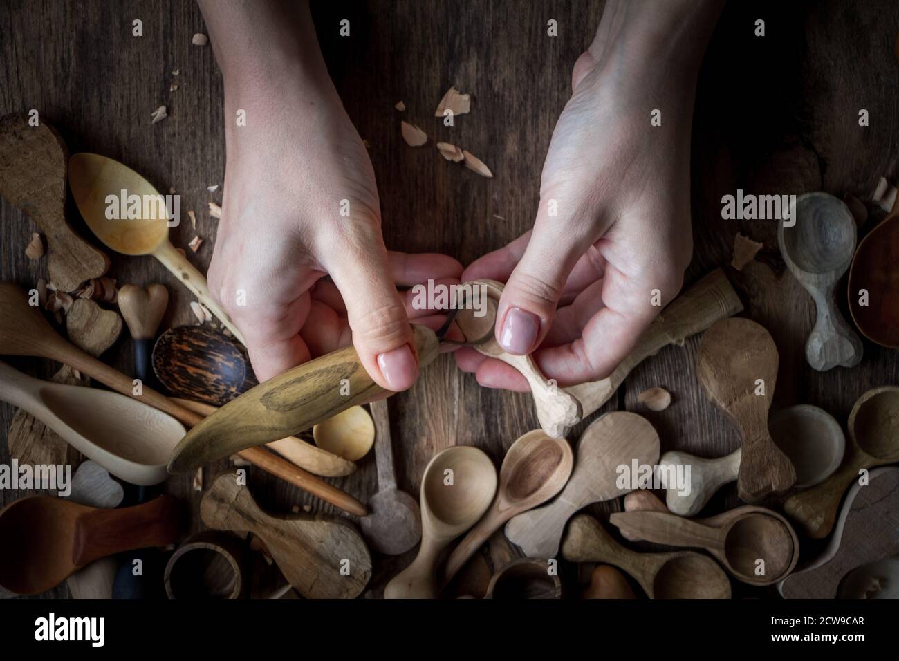 Handmade wooden utensils, top view female hands carve a wooden spoon with stock-knife, selective focus Stock Photo
