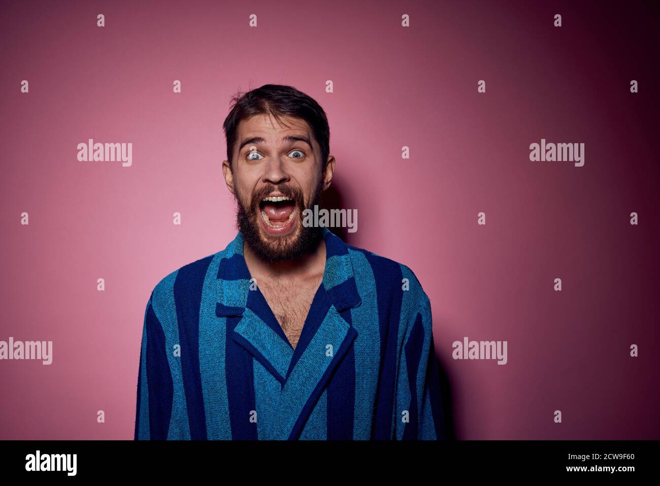 Bearded man in a blue striped robe on a pink background with hands ...