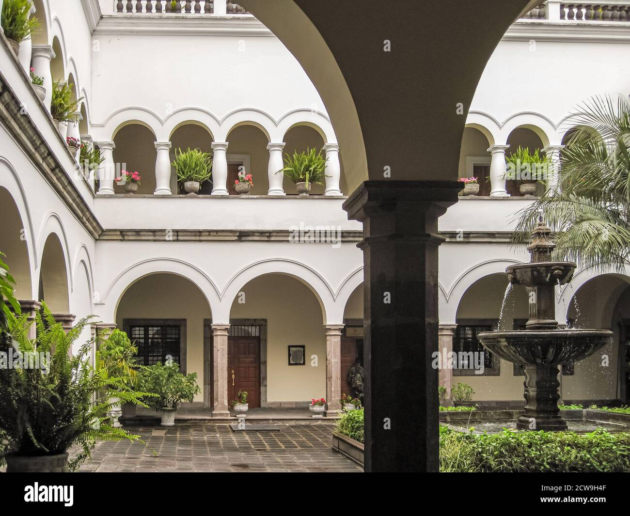 Quito, Ecuador - December 2, 2008: Inner courtyard with green foliage and fountain of Presidential Carondelet Palace. White walls with colonnade. Stock Photo