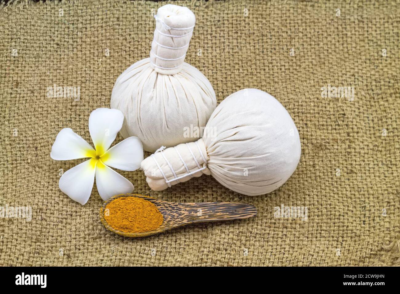 Spa herbal compressing ball , white frangipani flowers (Plumeria spp , Apocynaceae, Pagoda tree, Temple tree) and turmeric powder  in wooden spoon on Stock Photo