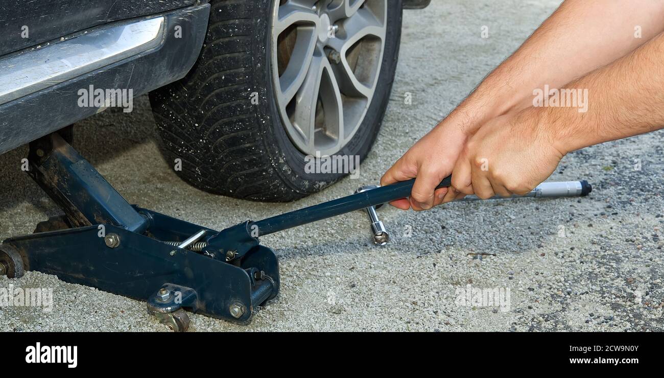 Man changing wheel. tire changer changing flat car tire. Help on road concept. Mechanic hands unscrews a flat tire of a car raised on a jack Stock Photo