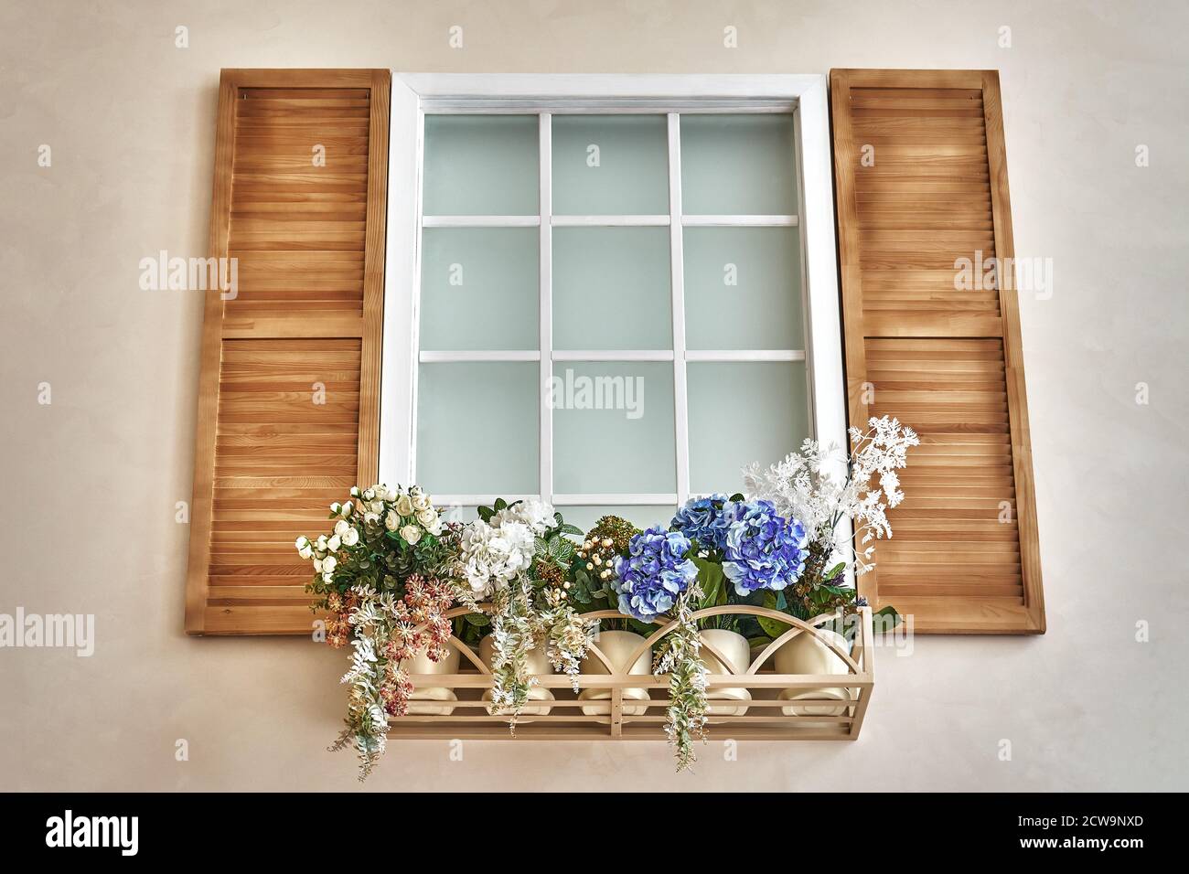 Faux interior window with wooden shutters and blooming flowers in ornamental flowerpot Stock Photo