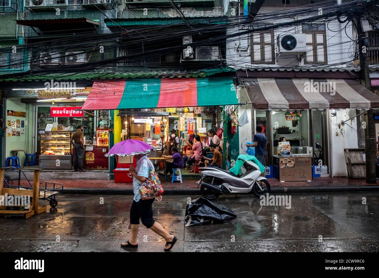 A man walks down the street with a small purple umbrella in Bangkok's Chinatown. Stock Photo