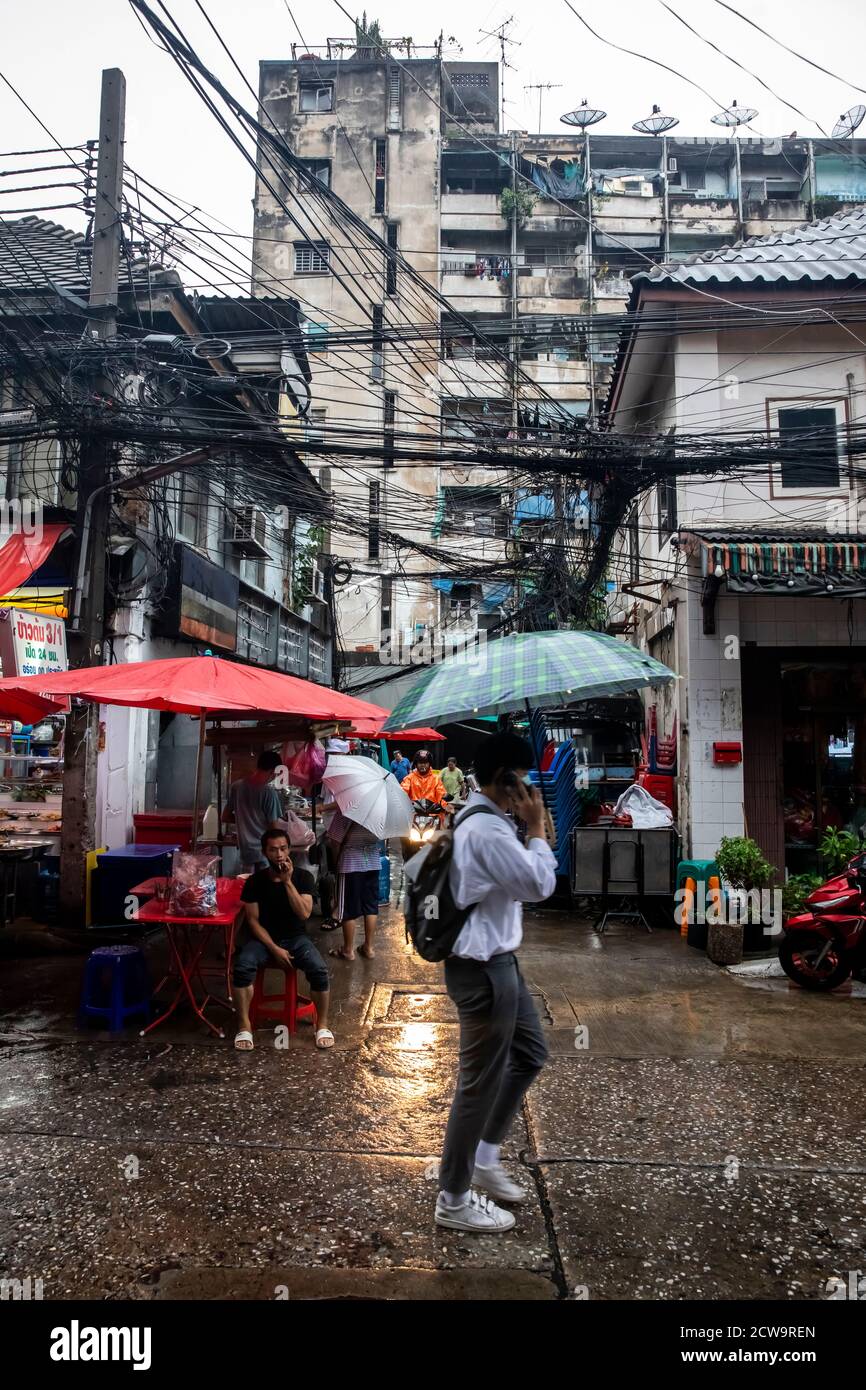 A commuter with cell phone and backpack heads home under an umbrella on a rainy evening in Bangkok's Chinatown. Stock Photo