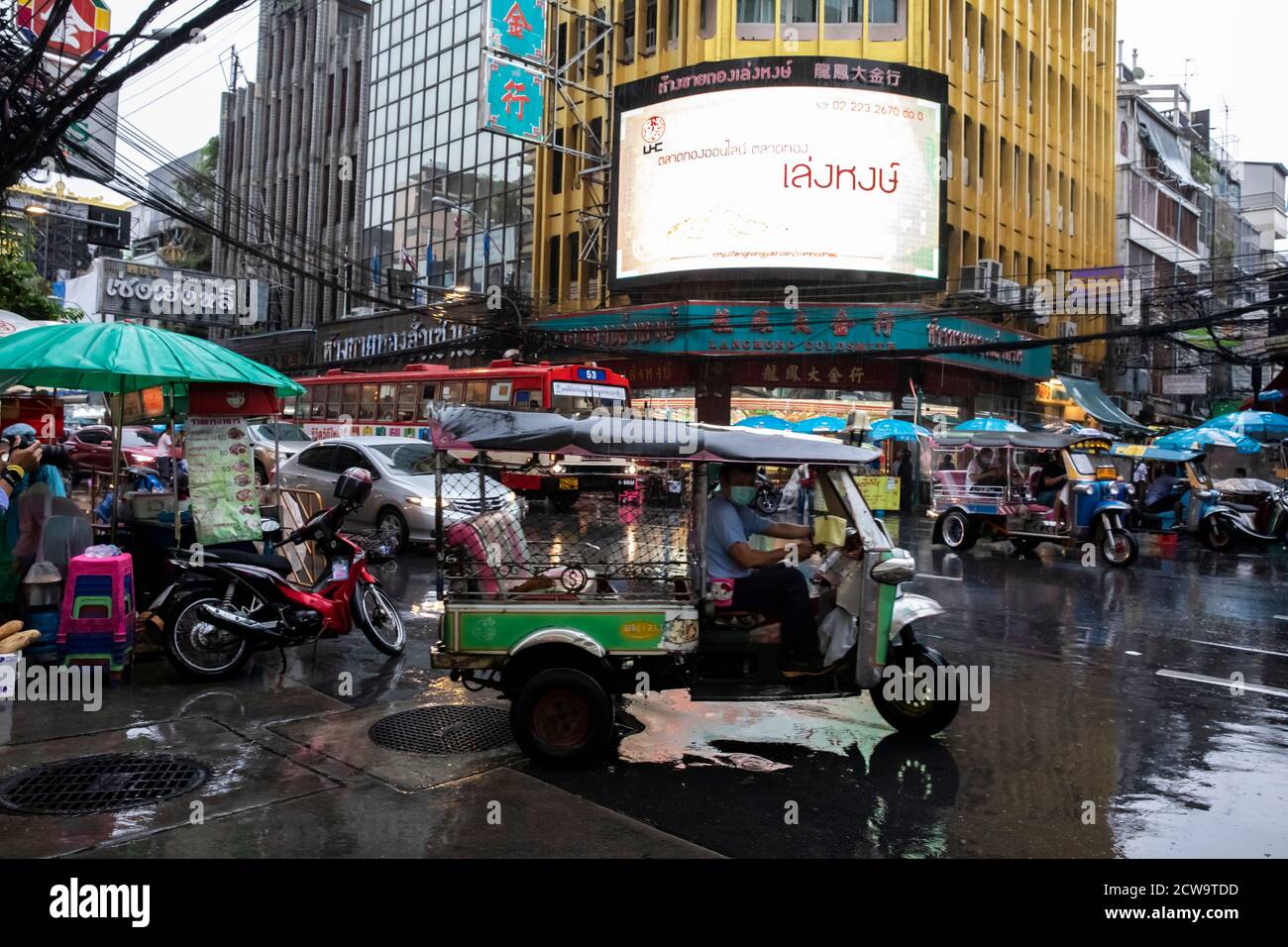 Cars, motorbikes, tuk tuks and pedestrians try to make their way during a rain storm in Bangkok's Chinatown. Stock Photo