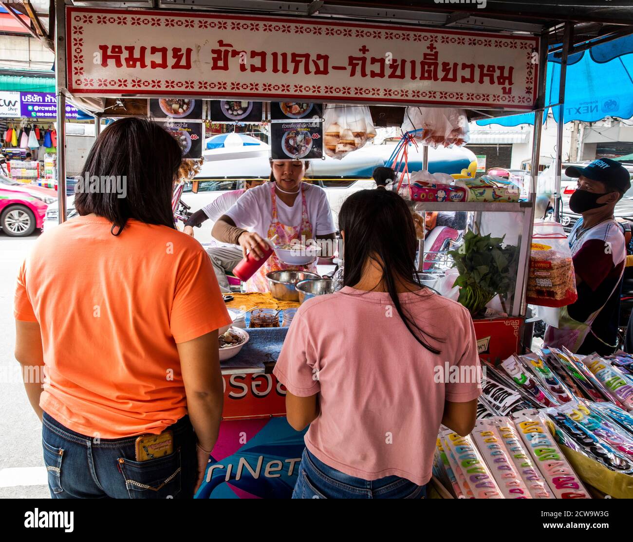 Two women wait for food at a vendor in Bangkok's Chinatown. Stock Photo