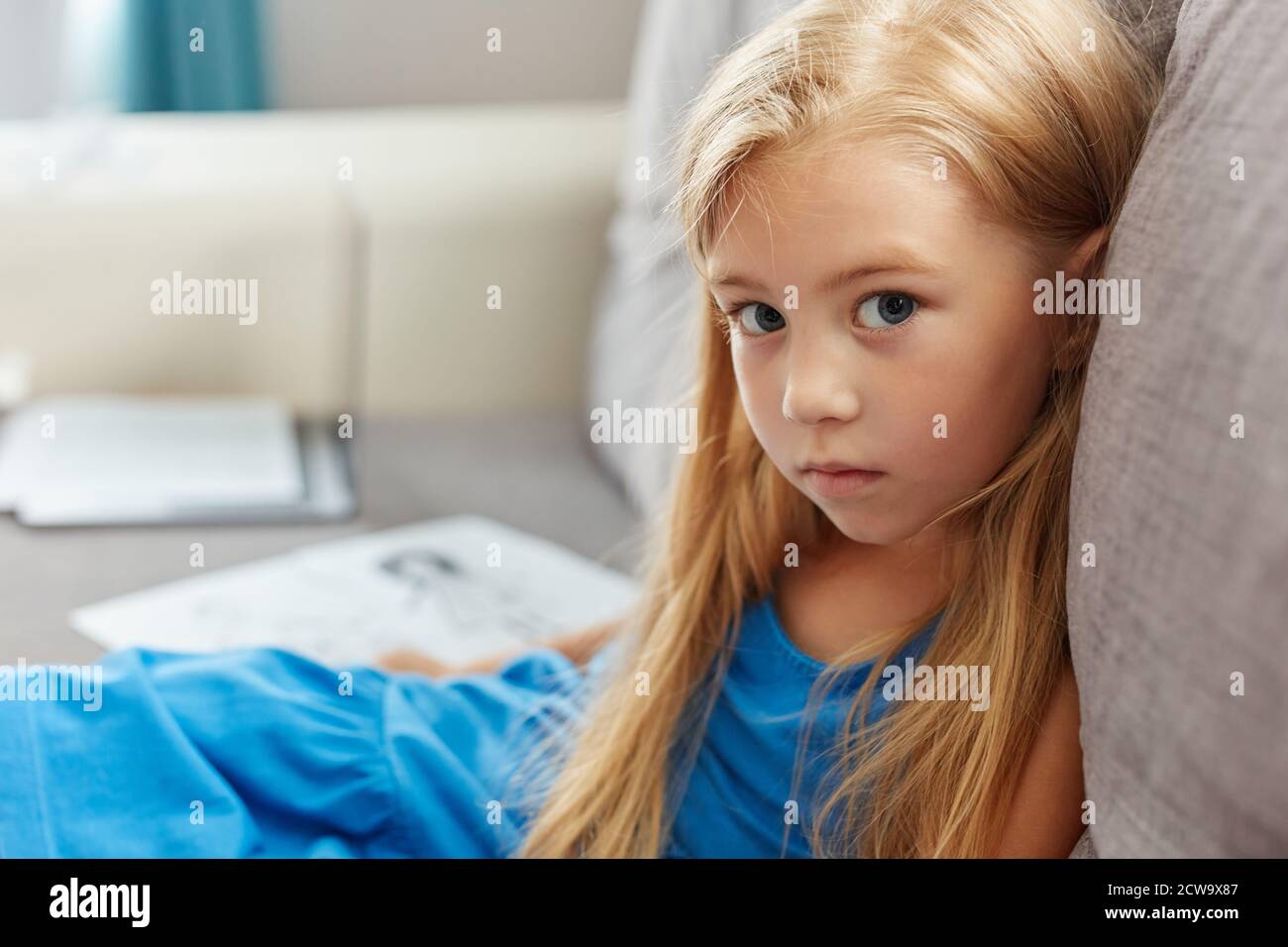 portrait of caucasian child girl in dress sitting on sofa in living ...