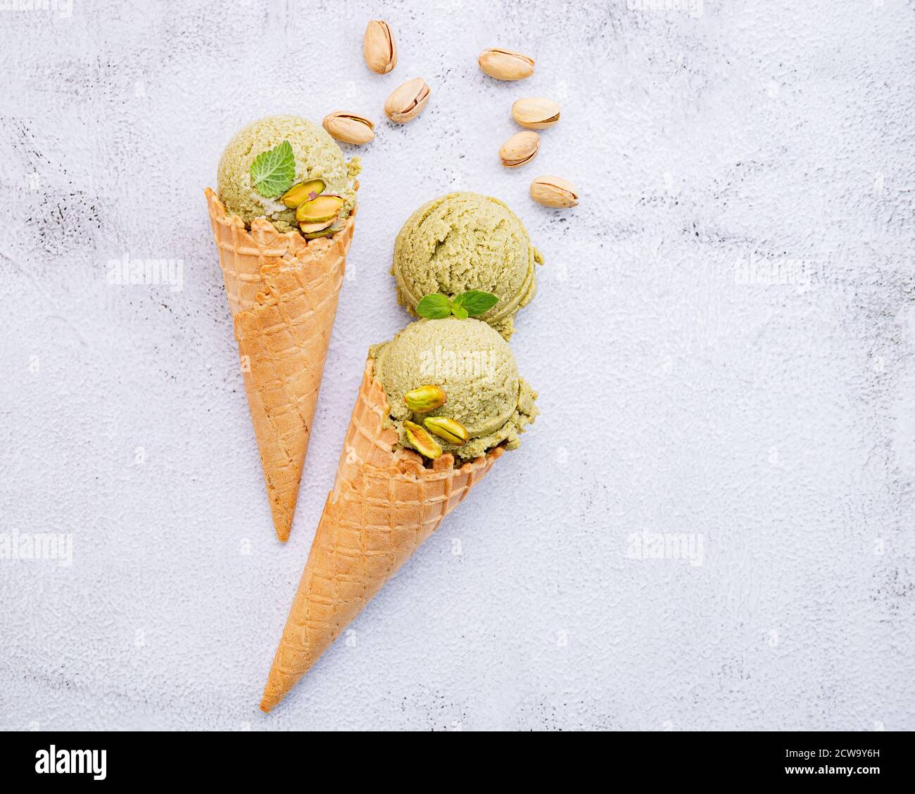 Pistachio ice cream in cones with pistachio nuts setup on white stone background . Summer and