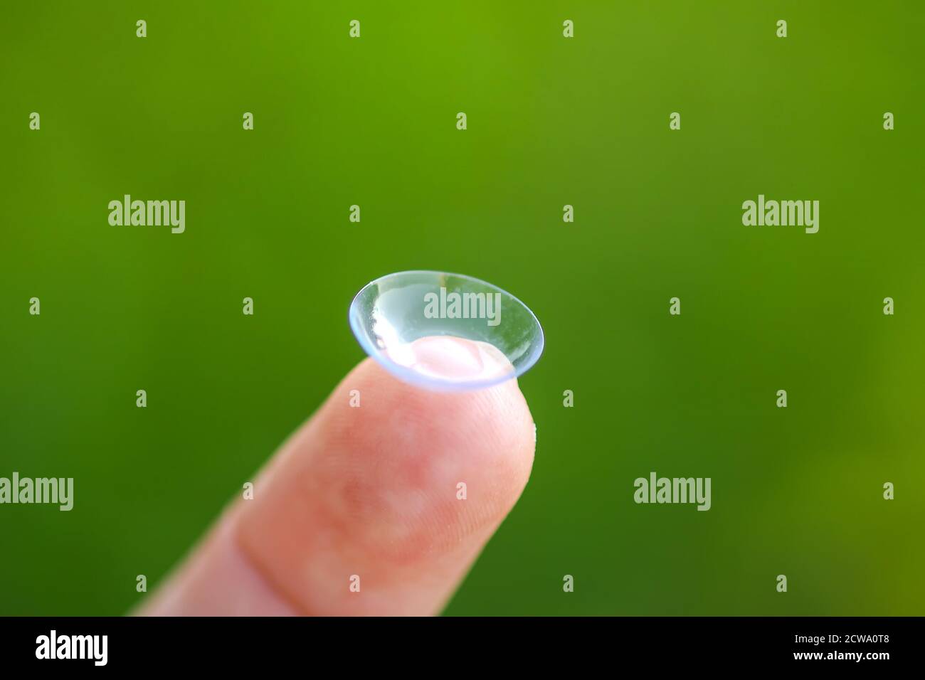 Transparent contact lens on finger tip on blurred green summer nature background. Stock Photo