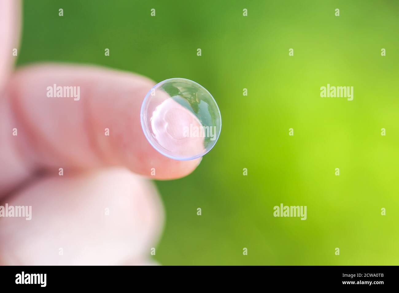 Transparent contact lens on finger tip on blurred green summer nature background. Stock Photo