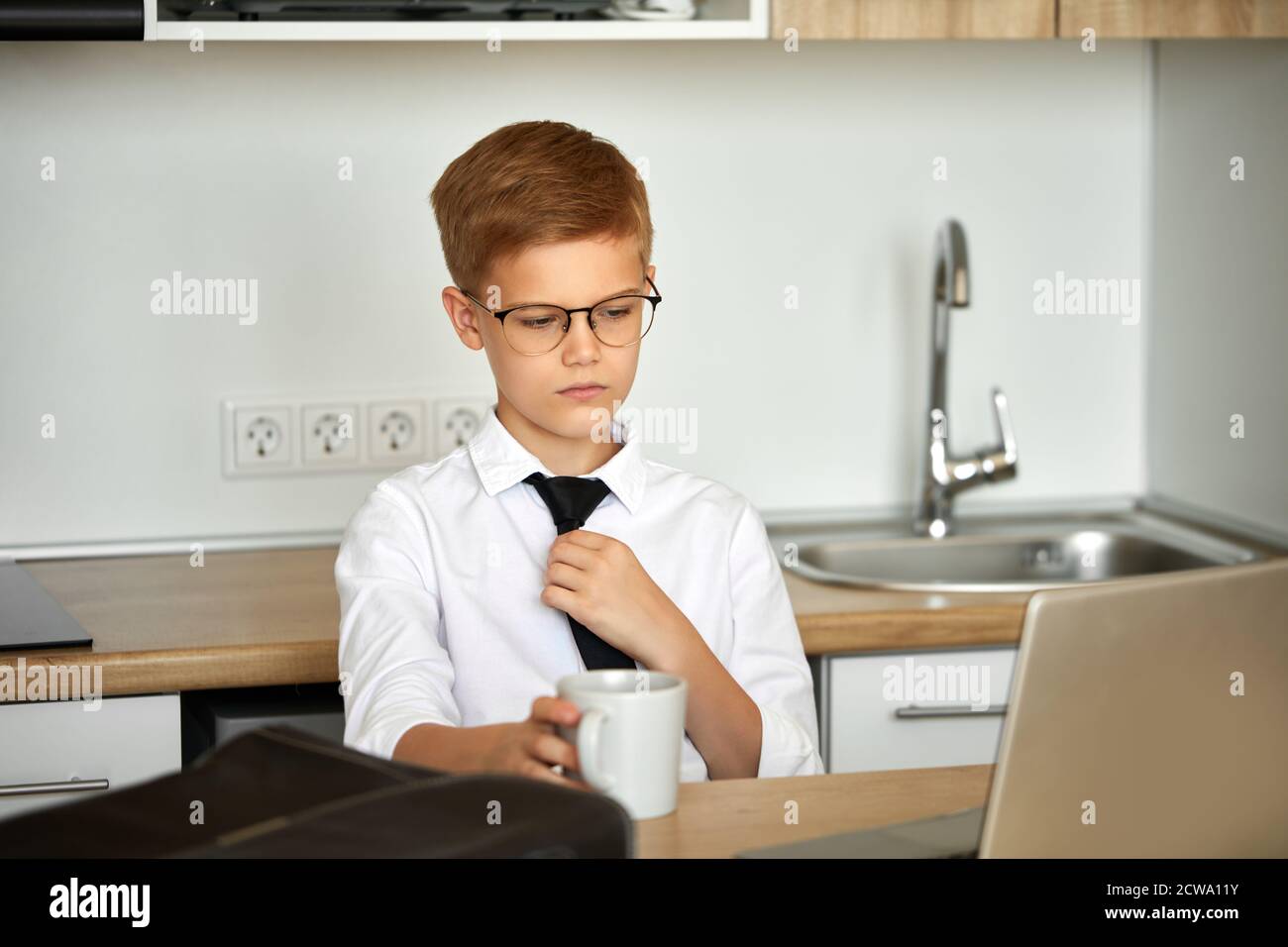 young caucasian business boy work from home using laptop, he is in formal wear, suit, in eyeglasses. intelligent boy is pretend to be adult Stock Photo