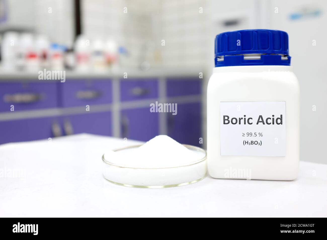 Selective focus of a bottle of pure boric acid chemical compound beside a petri dish with solid crystalline powder substance. White Chemistry laborato Stock Photo