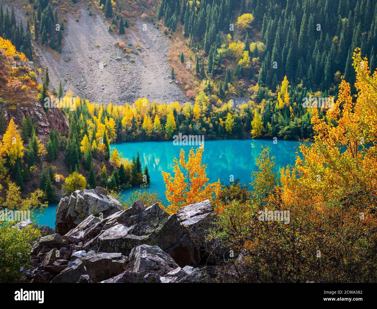 Autumn mood view of the Issyk mountain lake. The turquoise lake is surrounded by mountains with yellowed trees. Stock Photo