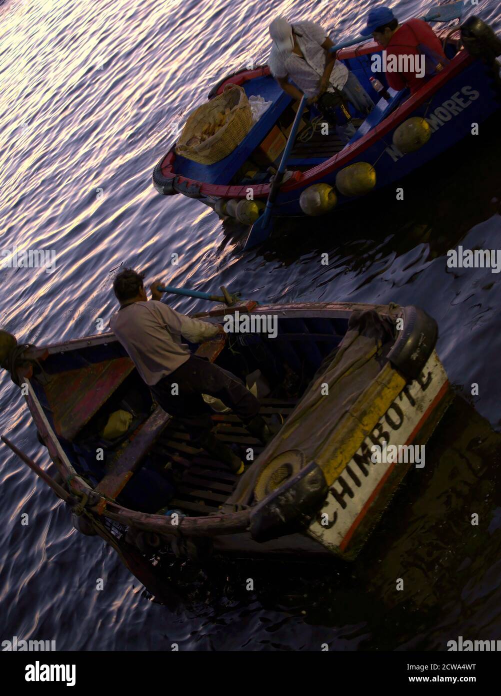 Chimbote, Peru - April 17, 2018: Men in small boats preparing to transfer to trawlers for night fishing on trawlers with trawlers and mountains in bac Stock Photo
