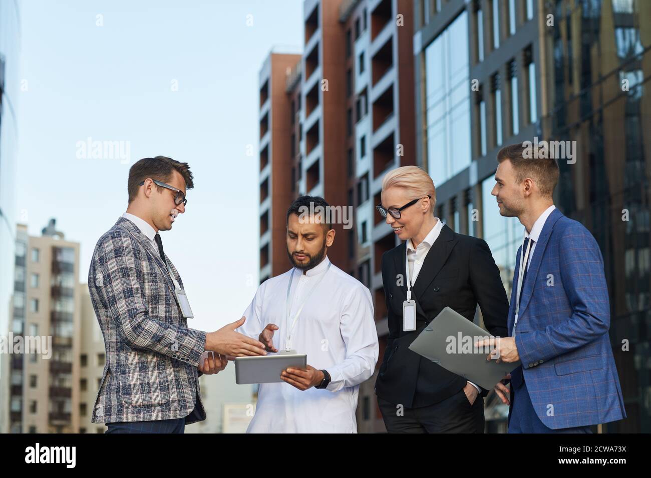 Businessman using digital tablet and discussing online presentation with his colleagues while they standing in the city outdoors Stock Photo